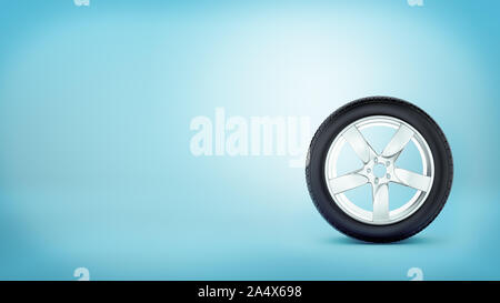 3d rendering of car wheel with five spokes standing on the tire rim on blue background. Stock Photo