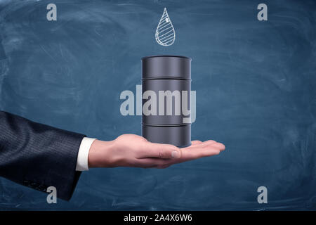 A businessman's hand turned up and a small black oil barrel standing on it with a drawn drop on chalkboard. Stock Photo