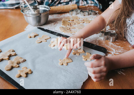 Young girl putting gingerbread man on baking tray