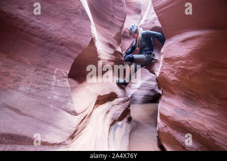 A woman canyoneer stems across a water-filled pothole in slot canyon Stock Photo