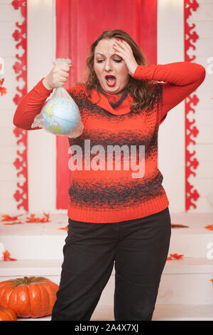 an emotional adult woman holds a planet in a plastic bag in her hands and shows irresponsible excessive consumer plastic. Stock Photo