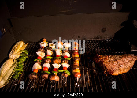 Corn and kabobs and a giant tri tip steak cook on a bbq at night. Stock Photo