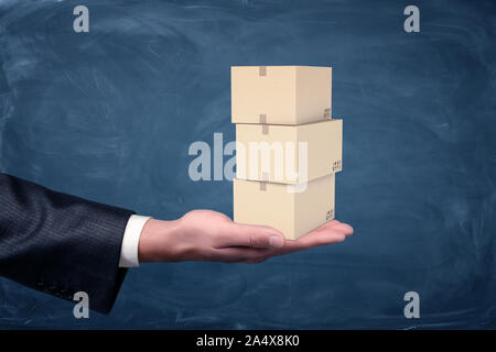 A businessman's hand holding a set of small three cardboard boxes palm up on chalkboard background. Stock Photo