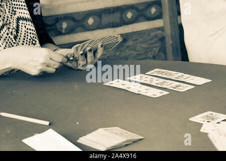 Sepia toned aged image effect  of womans hand with painted nails holding the cards playing card during day in Greek hill village bar. Stock Photo