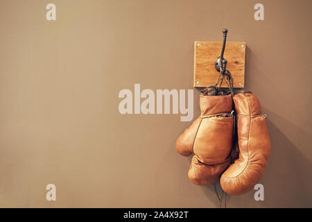 Museum of box sport. Box exhibition retro attributes. Boxing school. Vintage boxing gloves hang on hook wall background. Boxing gloves and copy space on grey. Finished boxing career famous sportsman. Stock Photo