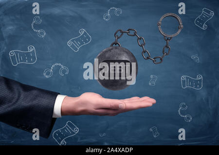 A businessman's hand turned palm up under a large hovering iron ball with a word DEBT written on it. Stock Photo