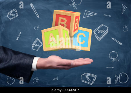 A businessman's hand turned palm up with big ABC blocks hovering above it. Stock Photo