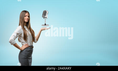 A long haired businesswoman holds out his hand for a metal retro microphone. Stock Photo