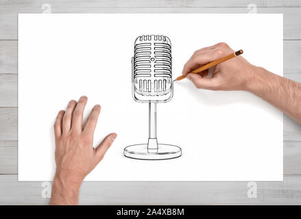 A pair of male hands in close view draws the retro microphone on a short stand with a pencil on white paper. Stock Photo
