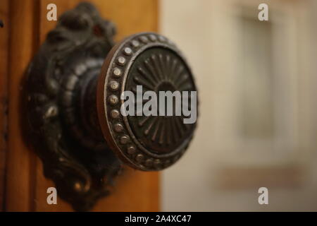 Round iron handle with a pattern on an old wooden door, closeup. Background in blur of a building with a window. Stock Photo