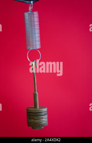 Masses hanging on a stretched spring isolated on a red background. School science experiment on Hooke’s law in a Physics laboratory Stock Photo