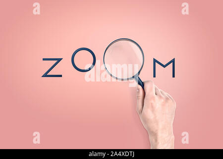 Male hand holds a large magnifying glass which serves as a letter in a word ZOOM. Stock Photo