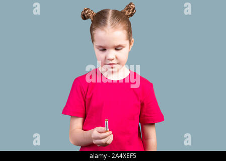 Little girl holds a cigarette in her hands and thinks. On a gray background. Stock Photo
