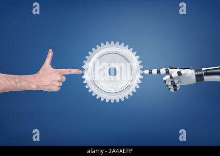A large metal spur gear with a human and a robotic hand touching it from different sides. Stock Photo