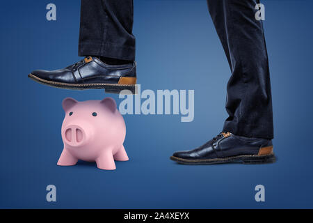 A pink piggy bank stands under a dangerous male foot which is ready to step on it.