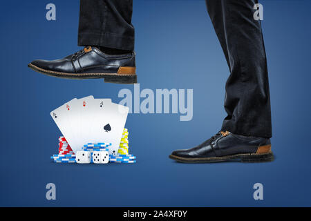 Businessman's shoes stepping on pack of cards, dice and stacks of chips on blue background. Stock Photo