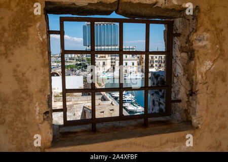 View of harbour through barred opening in wall of Angevine-Aragonese Castle in Gallipoli old town, Apulia (Puglia) in Southern Italy Stock Photo