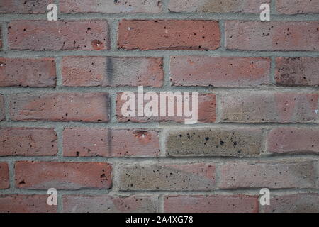 Head-on view of a modern, red brick wall with worn damage. Stock Photo