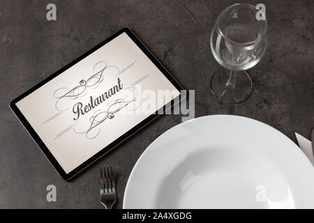 Tablet with stylish restaurant logo and laid table Stock Photo