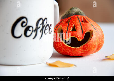 https://l450v.alamy.com/450v/2a4xgp0/ceramic-orange-small-smile-halloween-pumpkin-with-autumn-leaves-near-it-and-coffee-cup-with-text-coffee-on-it-holiday-concept-2a4xgp0.jpg