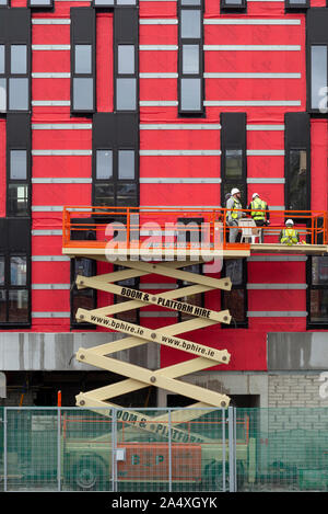 Workers or builders on a cherry picker or boom platform at the Horgan's Quay red building construction site in Cork City, Ireland. Stock Photo