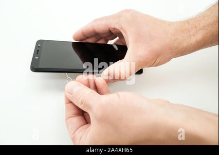A man is holding a smartphone. He is using a pin to open the slot for a SIM card. Stock Photo