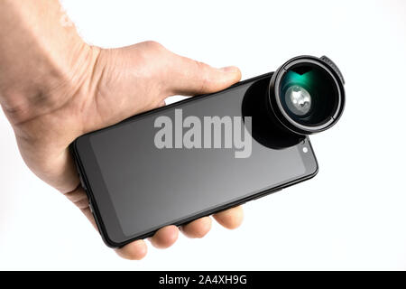 The human hand is holding a smartphone with an attached external lens. Stock Photo