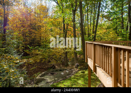 Home in the autumn woods showing fall foliage, section of a large deck, and a fire pit.  Outdoor living concept. Stock Photo