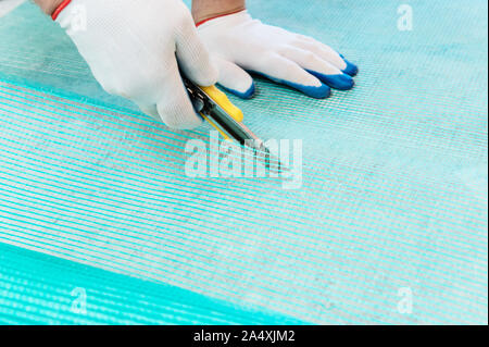 A worker is cutting off a piece of fiberglass mesh with a knife. Stock Photo
