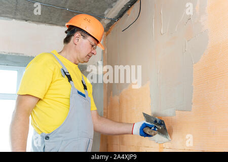 The worker is applying putty on a fiberglass mesh on the wall. He is using a trowel. Stock Photo