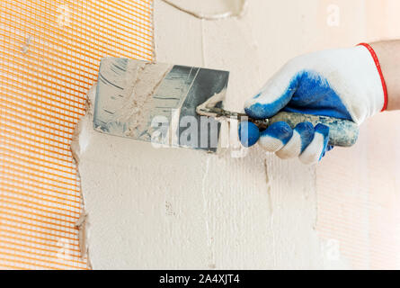 A worker is applying plaster to the mash on the wall with a trowel. Stock Photo