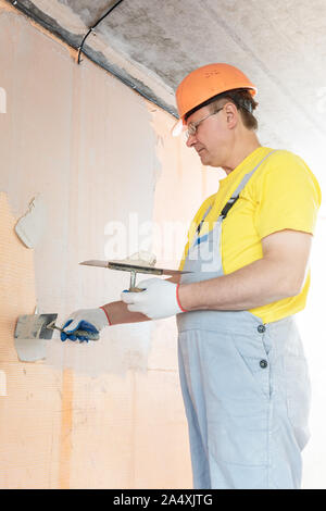 The worker is applying putty on a fiberglass mesh on the wall. He is using a trowel. Stock Photo