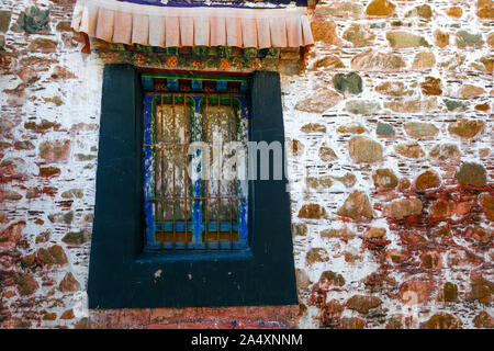 A brightly painted rock wall surrounds a decaying window at Deprung Monastery in Lhasa, Tibet. Stock Photo