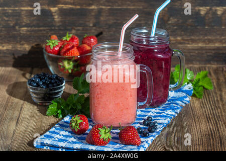 Summer berries smoothie in mason jar on rustic wooden table. Healthy cocktails with fresh fruits. Close up two drinks and fresh berry Stock Photo