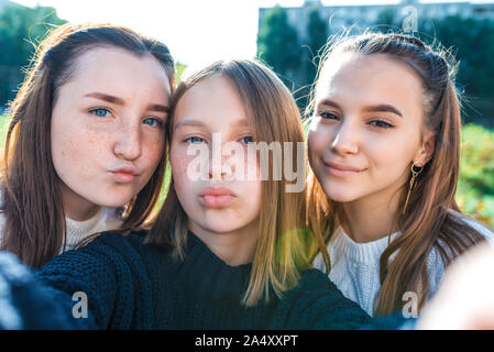 Three girls schoolgirls girlfriends kissing video camera smartphone. They take pictures themselves with camera. They transmit video call, online app Stock Photo