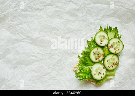 Open sandwich on a sheet of green fleece with cucumber and flax seed on wafer bread on a light paper background. top view. Copy space. Stock Photo