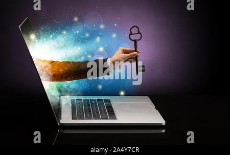 Hand with huge vintage key coming out of a laptop with sparkling effects Stock Photo