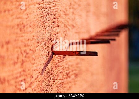 a row of metal sticks protruding from the orange concrete wall may be for defense or assembly Stock Photo