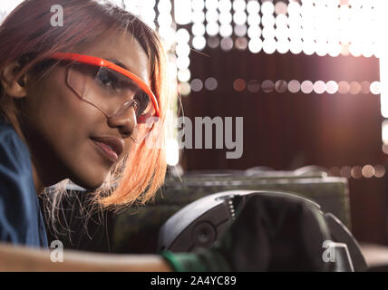 Diverse female mechanical engineer operating heavy industrial machinery - Dark skin Asian woman working in engineering workshop wearing safety glasses Stock Photo