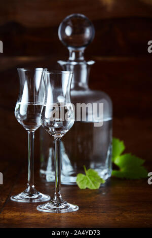 Two grappa glasses and decanter, decorated with green grape leaves on dark brown background Stock Photo
