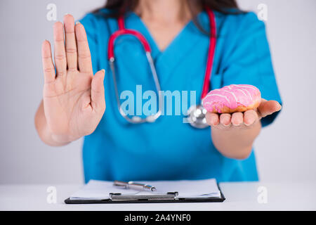 Healthy lifestyle, food and sport concept. Doctor woman hand holding donut or unhealthy food and outstretched hand showing stop sign green apple. Stock Photo