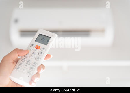woman hand holding remote controller directed on the air conditioner inside the room and set at ambient temperature,25 degrees celsius. Stock Photo