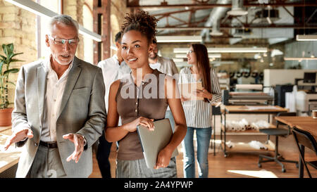 Sharing ideas. Two business experts discussing something while walking with colleagues through the office corridor. Partnership. Teamwork Stock Photo