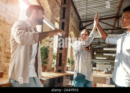 Give me five! Young man and woman giving high-five while having coffee break with colleagues in the modern office. Teamwork. Office life Stock Photo