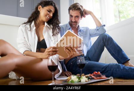 Romantic young couple relaxing together in bedroom,drinking wine and using tablet Stock Photo