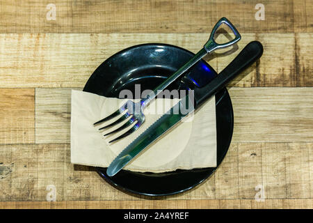 The fork and knife in a black plate with tissue paper on the wooden table Stock Photo