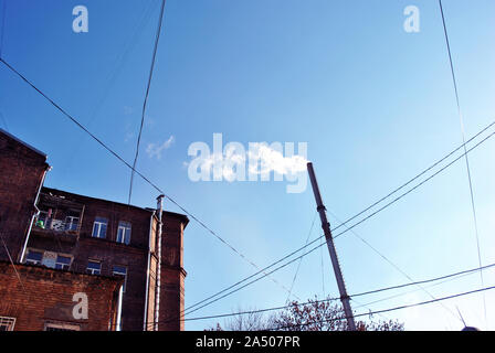 Old pipe with smoke, red brick building corner with windows and wires on winter bright blue sky background, view from ground on top Stock Photo