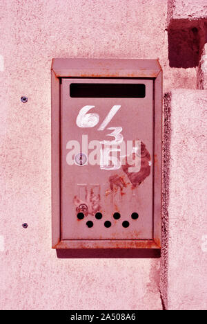 Red metal mailbox with white number painted on it, textured wall  grunge vertical shabby background Stock Photo