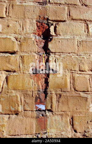 Cracked soft yellow paint, plaster surface on brick wall, grunge vertical shabby background detail close up Stock Photo