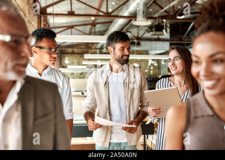 Office life. Modern business people discussing something and smiling while walking through the office corridor Stock Photo